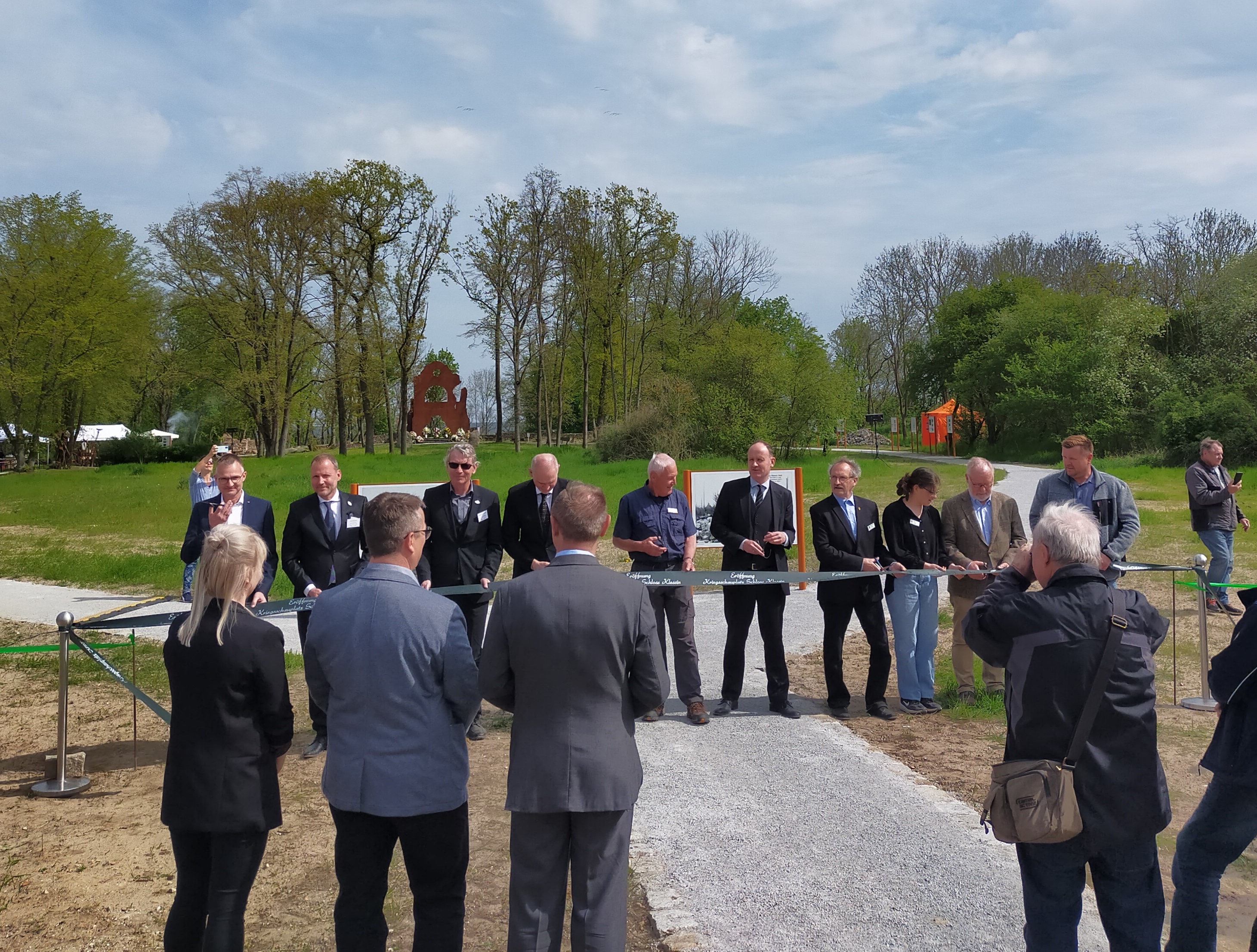 Vor dem Hintergrund des Rundweges um das ehemalige Schlossgelände sind zehn Personen im Begriff das Eröffnungsband durchzuschneiden