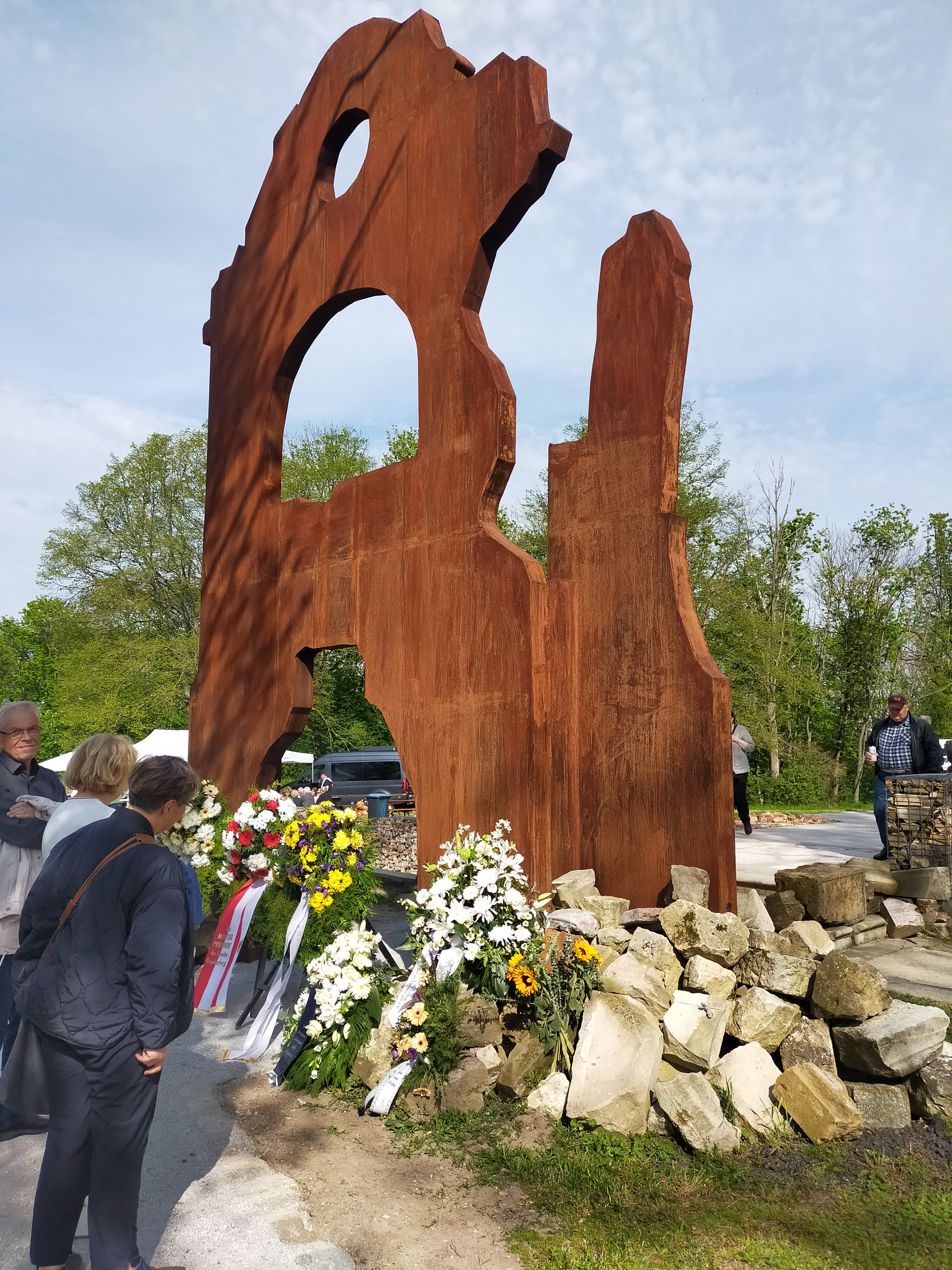 Die Nahaufnahme zeigt das nachgebildete Schlossportal. Menschen begutachten die Gedenkkränze am Fuß der Monumentalplastik 
