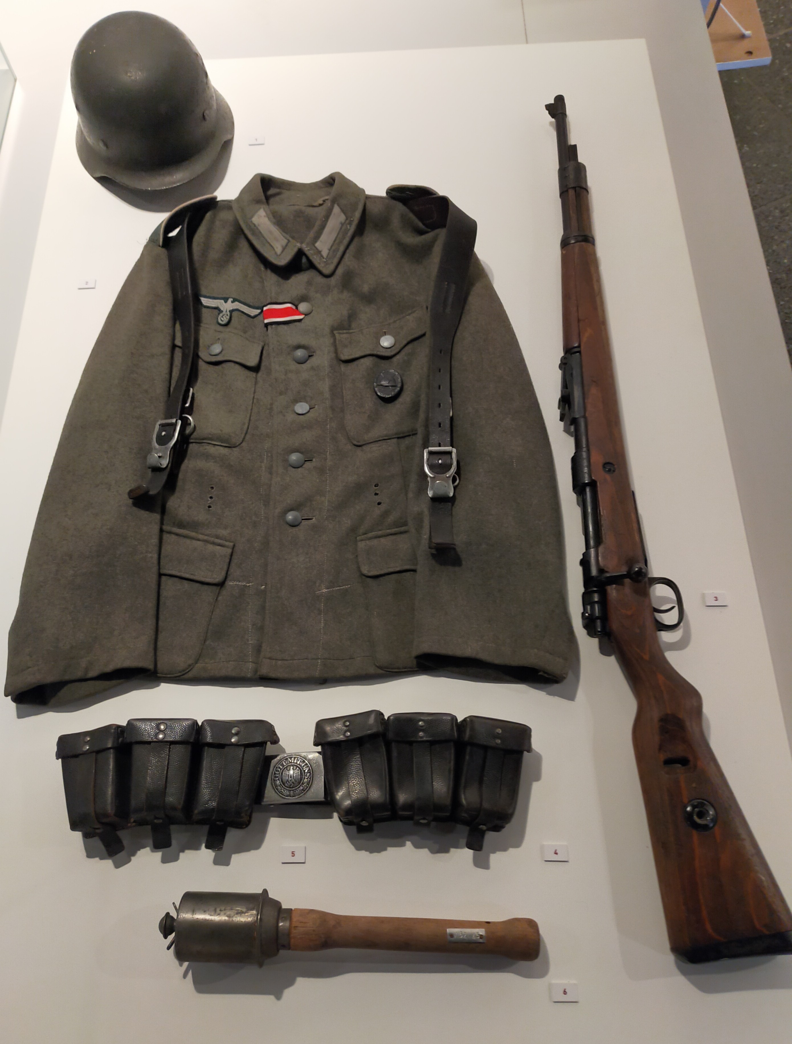 Die Präsentation eines Sets infanteristischer Ausrüstung umfasst Stahlhelm, Feldbluse, Karabinergewehr und Patronentaschen